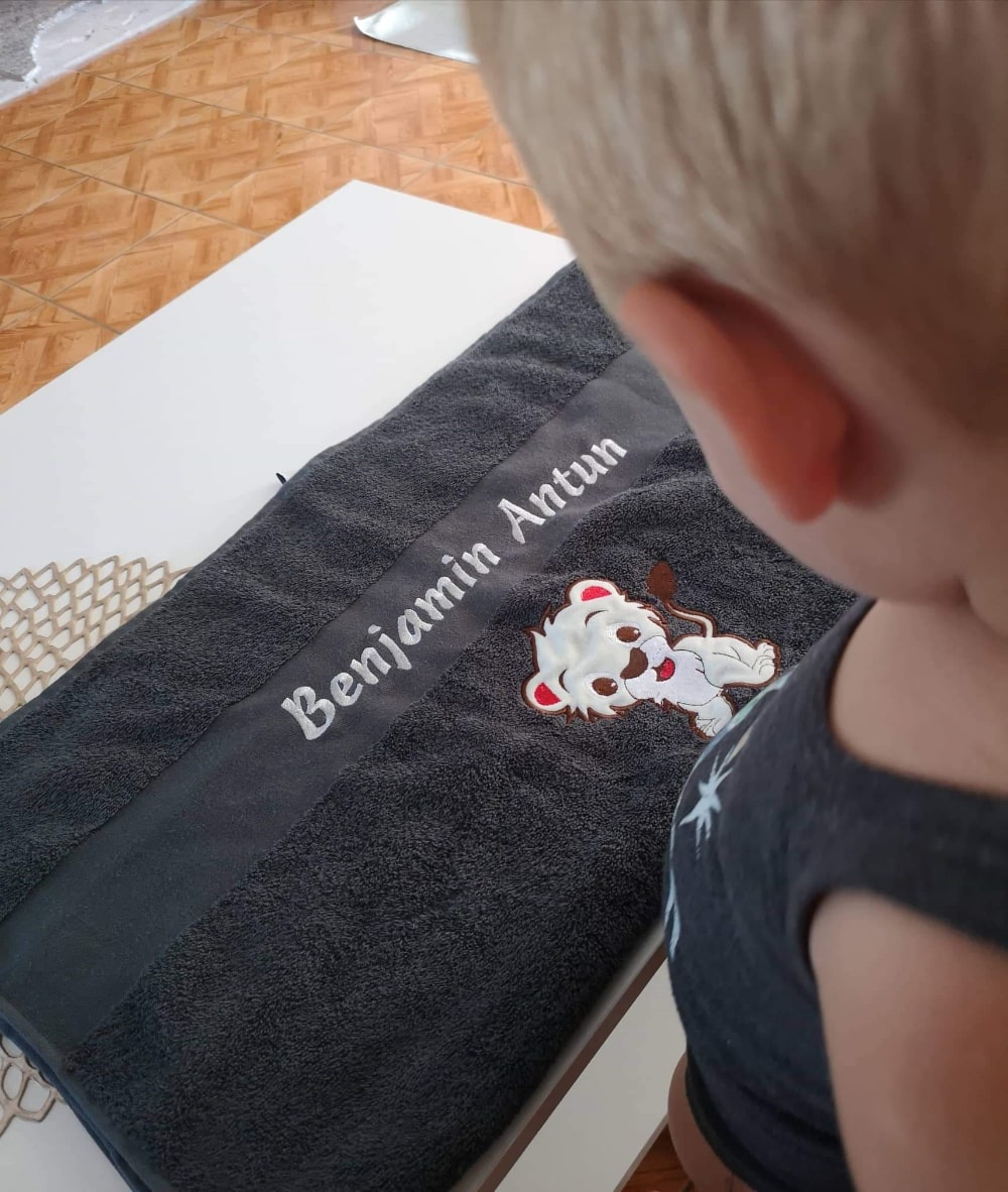 Dječak s ponosom pokazuje svoj personalizirani ručnik, s živopisnim dizajnom i svojim imenom.